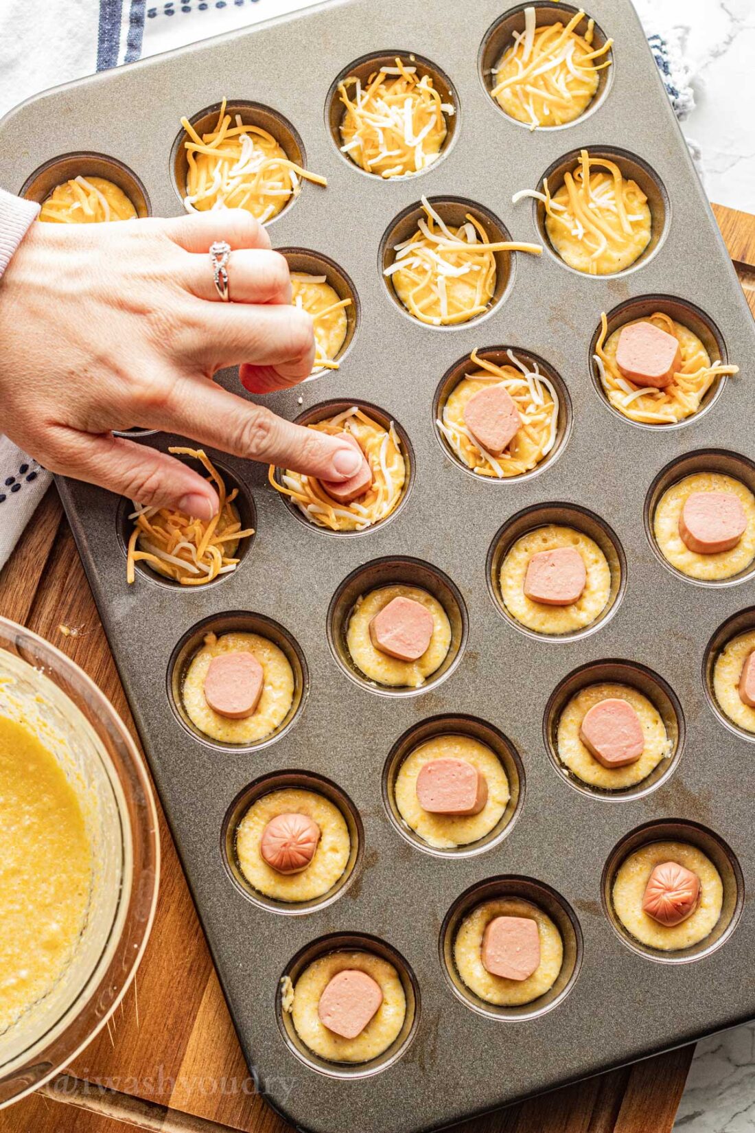 adding hot dogs and cheese to corn dog batter.