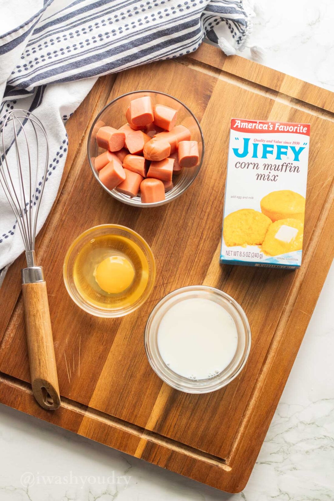 ingredients for mini corn dogs on wooden surface with whisk.