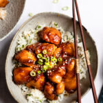 gray bowl with sesame chicken over rice and chopsticks on right side.