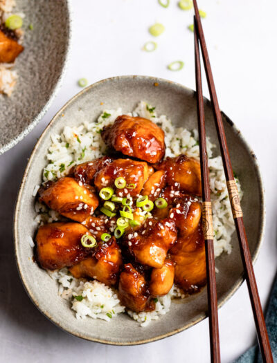 gray bowl with sesame chicken over rice and chopsticks on right side.