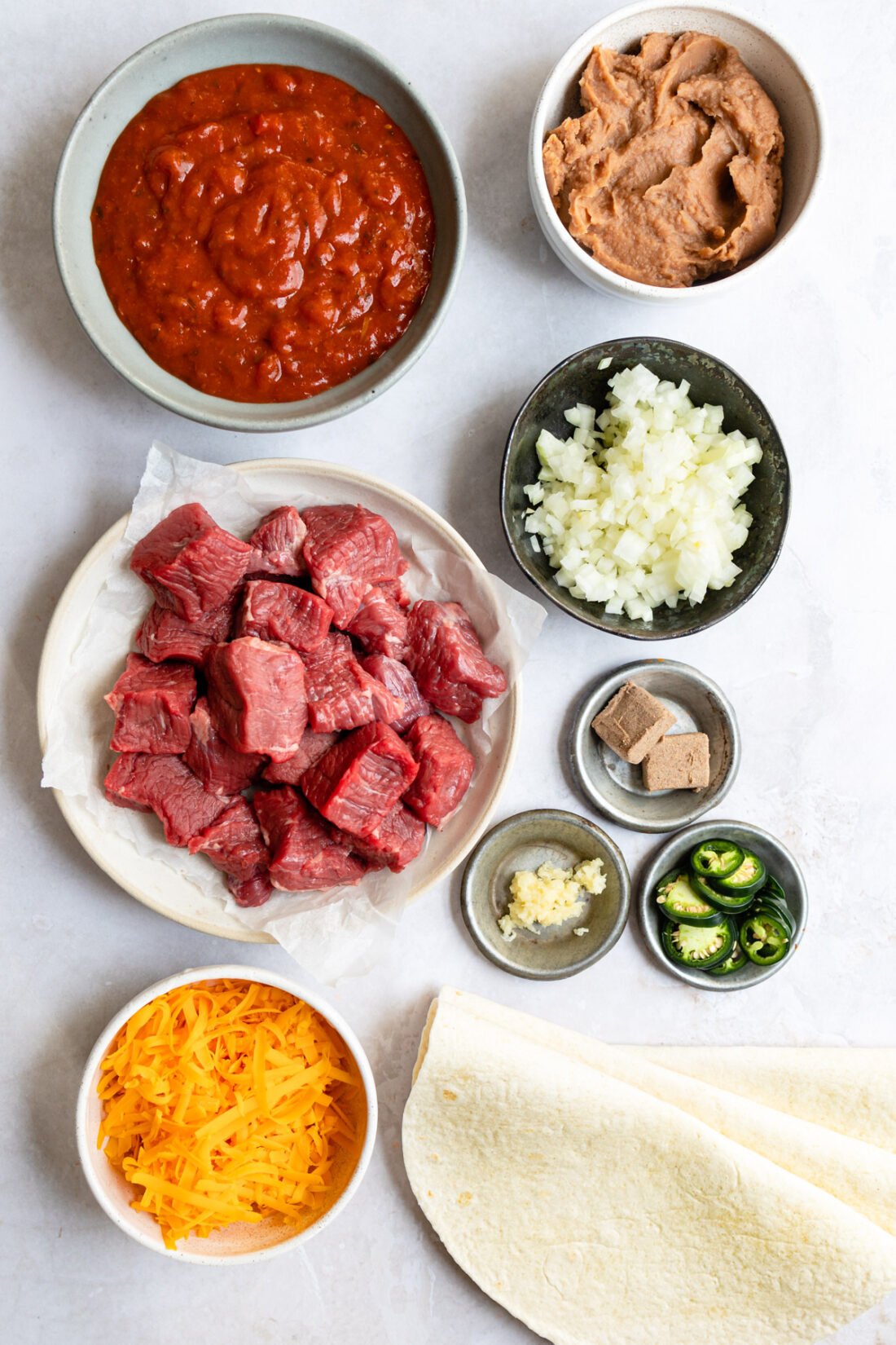 ingredients for crock pot smothered beef burritos on white surface.