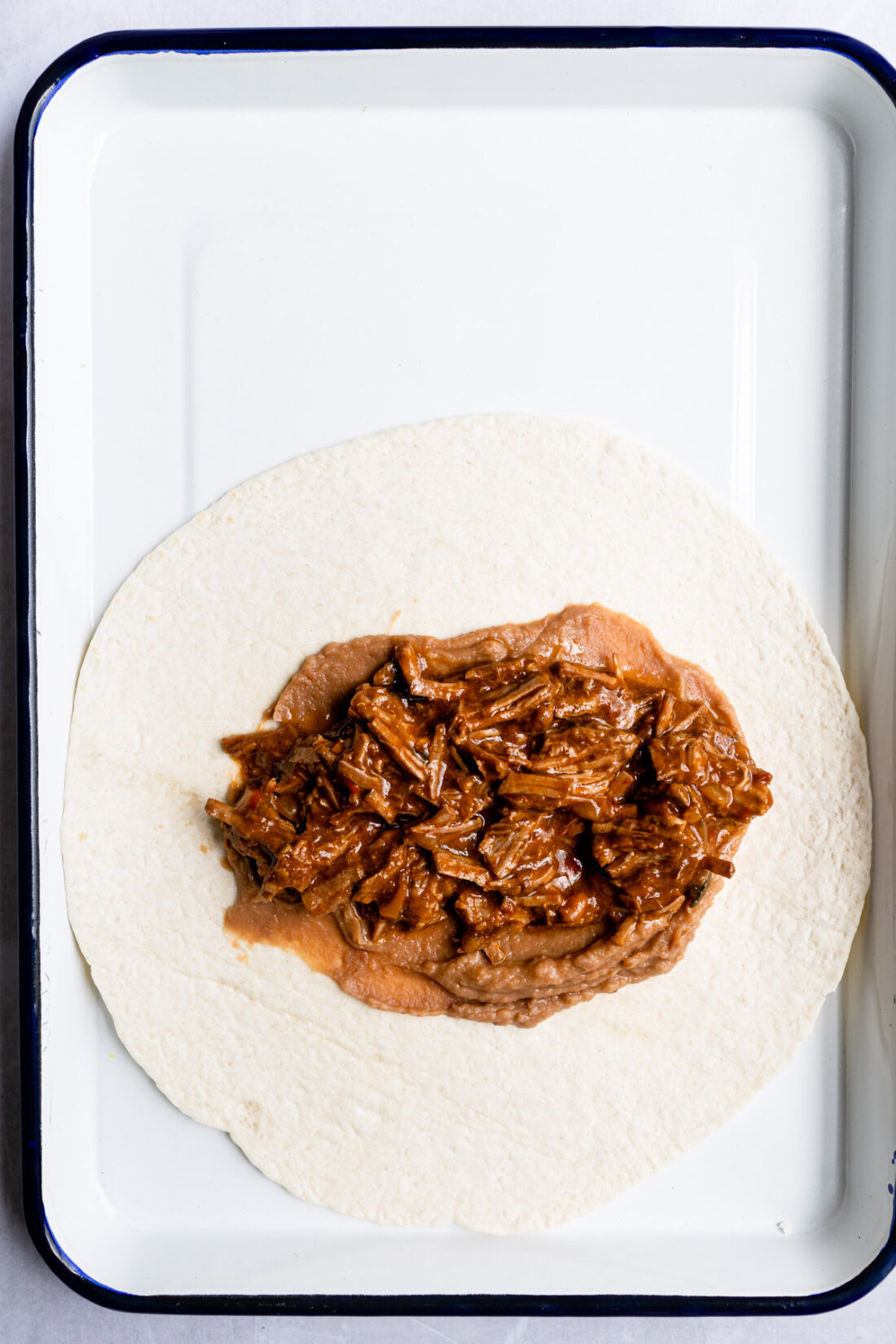 tortilla topped with refried beans and shredded beef on white surface. 