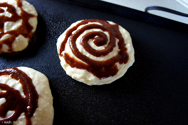 A close up of pancake batter on a skillet with a cinnamon swirl on top. 