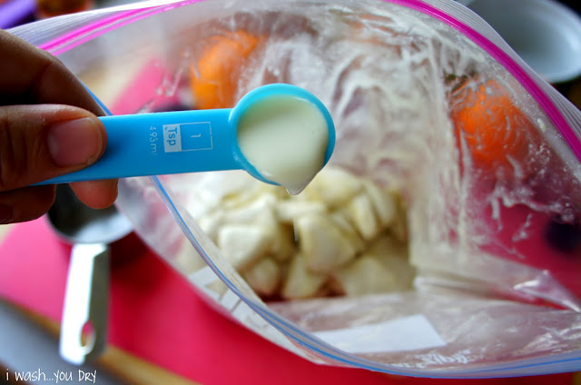 A hand holding a measuring spoon of liquid over a bag of dough