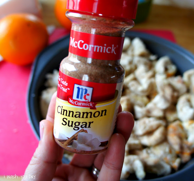 A hand holding a bottle of Cinnamon Sugar in front of a Orange Cinnamon Pull Apart in a round baking pan