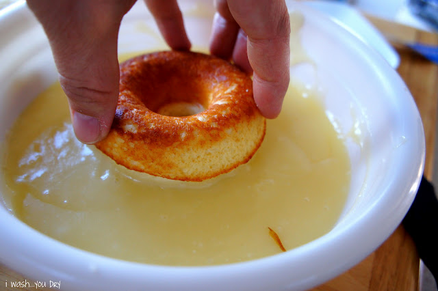 A hand holding the top of a donut in a bowl of glaze