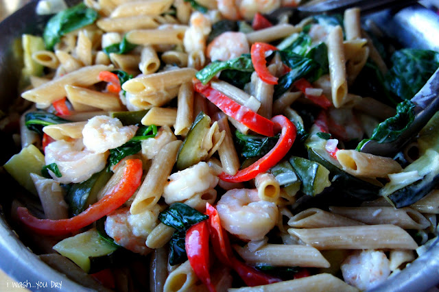 A close up of pasta, veggies, shrimp and cream sauce mixed together. 