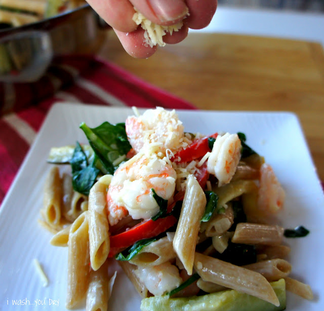 A hand sprinkling cheese on top of a plate of pasta with veggies and shrimp.