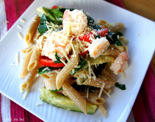 A close up of a plate of food, with pasta, shrimp, veggies and cream sauce.