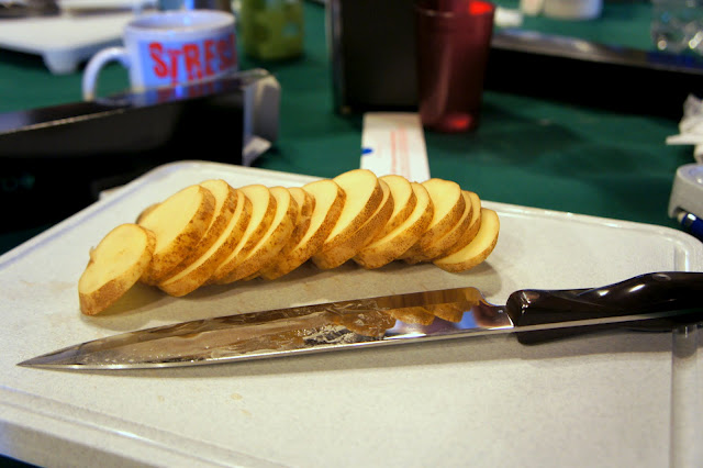 A cutting board with knife and sliced potatoes