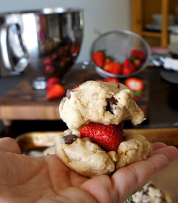 A hand holding a strawberry between two small balls of raw cookie dough