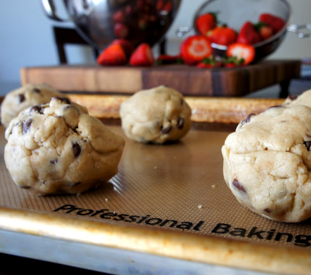 A close up of a pan with balls of raw cookie dough in front of a cutting board with strawberries on it