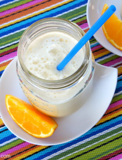 A close up look into a mason jar filled with Pineapple Orange Julius on a plate next to a slice of orange