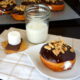 A Marshmallow Cream filled S'mores Doughnut displayed on a plate next to a glass of milk and an uncooked S'more