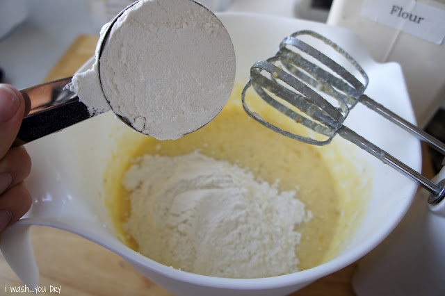 Flour being added to a mixing bowl with batter in it.