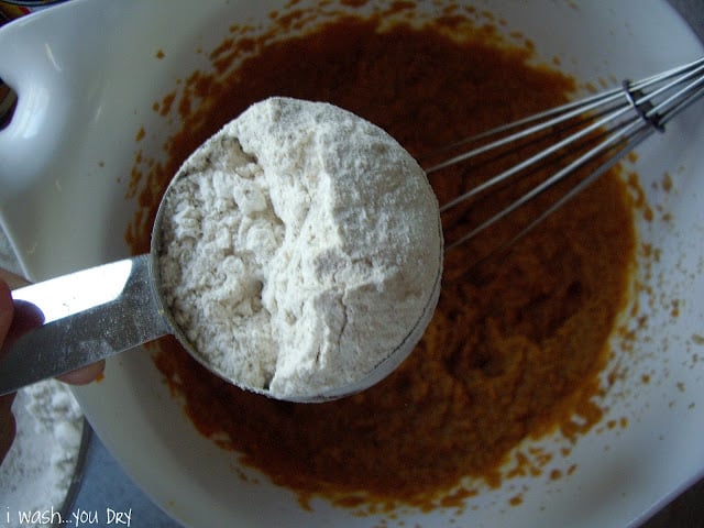 A measuring cup of flour above a bowl of batter. 