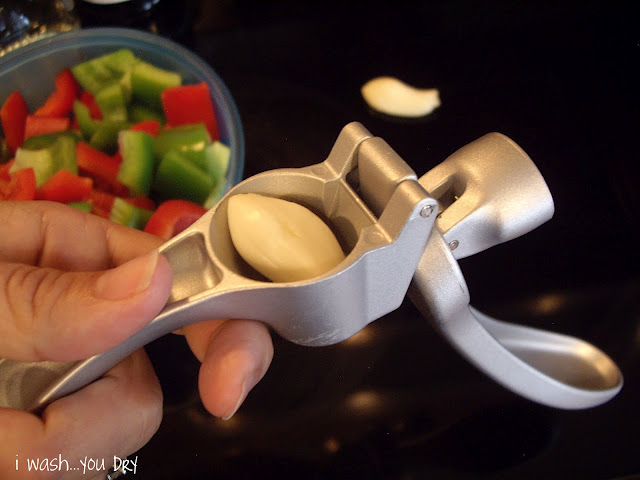 A hand holding a garlic press with a clove of garlic in it. 