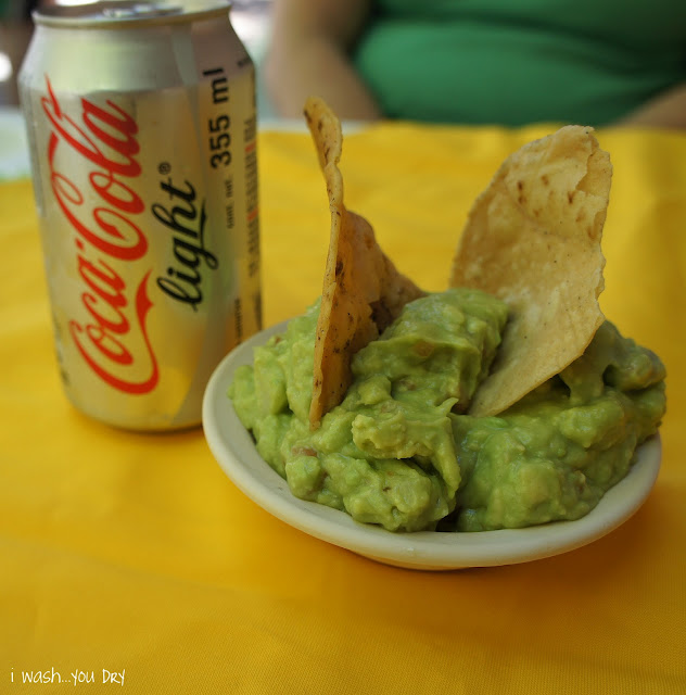 A can of Cocoa Cola Light next to a bowl of guacamole with two chips in it. 