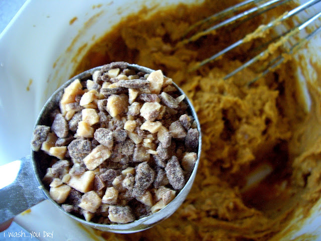 A measuring cup with toffee bits above a bowl of cookie batter. 