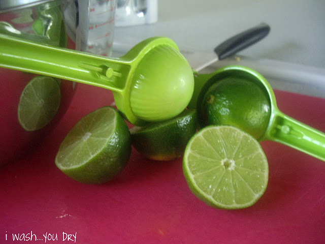 Lime halves on a cutting board next to a lime juicer. 