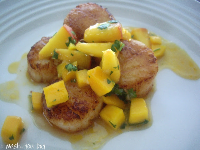 Scallops displayed on a plate topped with a mango and peach sauce. 