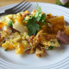 A plate of food on a table, with egg, ham and potatoes and cheese.