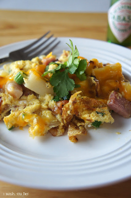 A plate of food on a table, with egg, ham and potatoes and cheese.