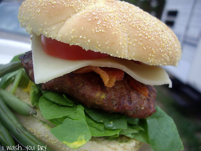 A close up of a burger, cheese, bacon, a tomato slice, and lettuce between two buns.