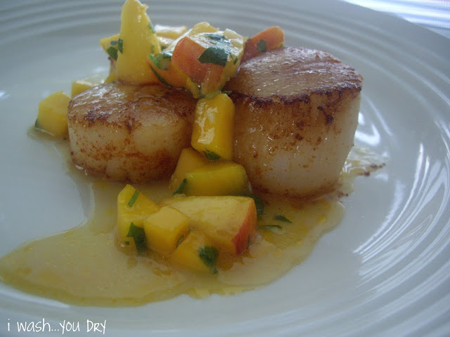 A close up of Scallops on a plate topped with a mango and peach sauce. 