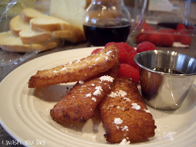 A display of french toast strips sprinkled with powdered sugar with a side of raspberries. 