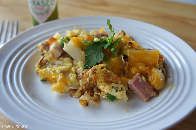 A plate of food on a table, with egg, ham and potatoes and cheese.