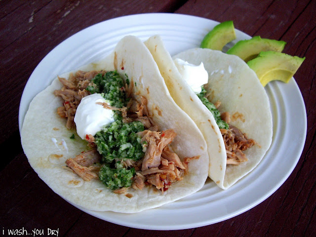 A display of two tacos on a plate with a side of avocado slices. 