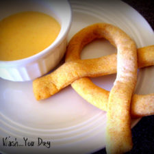 A homemade pretzel on a plate next to a small bowl of dipping sauce.