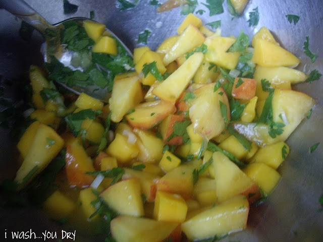 A spoon stirring a bowl with mango and peach salsa. 