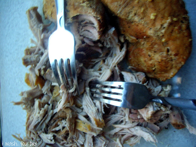 Two forks shredding pork on a cutting board. 