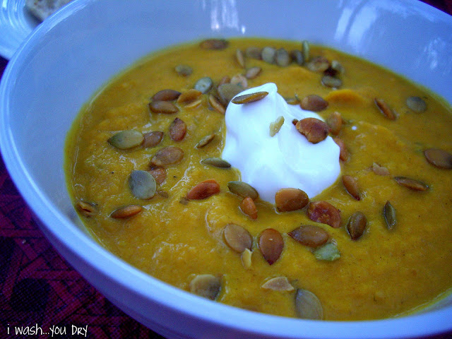 A close up of a bowl of soup topped with pumpkin seeds and sour cream. 