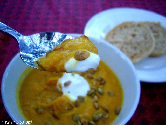 A spoon of soup above a display of food. 