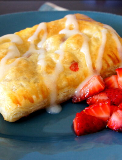 A close up of a Homemade Strawberry and Cream Cheese Toaster Strudel on a plate, with a side of diced strawberries