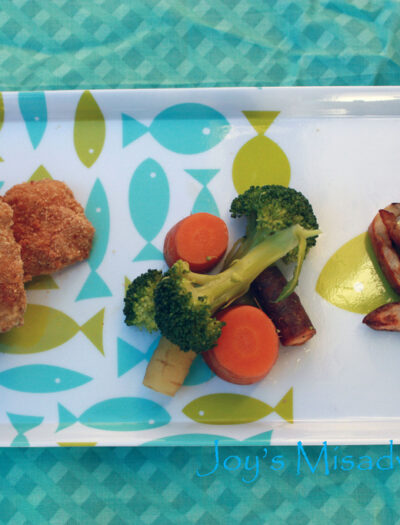 A plate of Cornbread Chicken Nuggets with a side of broccoli and carrots and potato fries