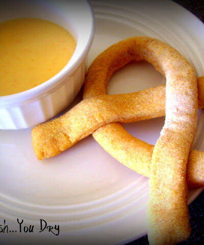 A homemade pretzel next to a bowl of dipping sauce.