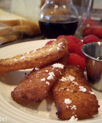 A display of french toast strips sprinkled with powdered sugar with a side of raspberries.