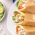 white plate with chicken souvlaki wrapped in pita bread with cucumbers.