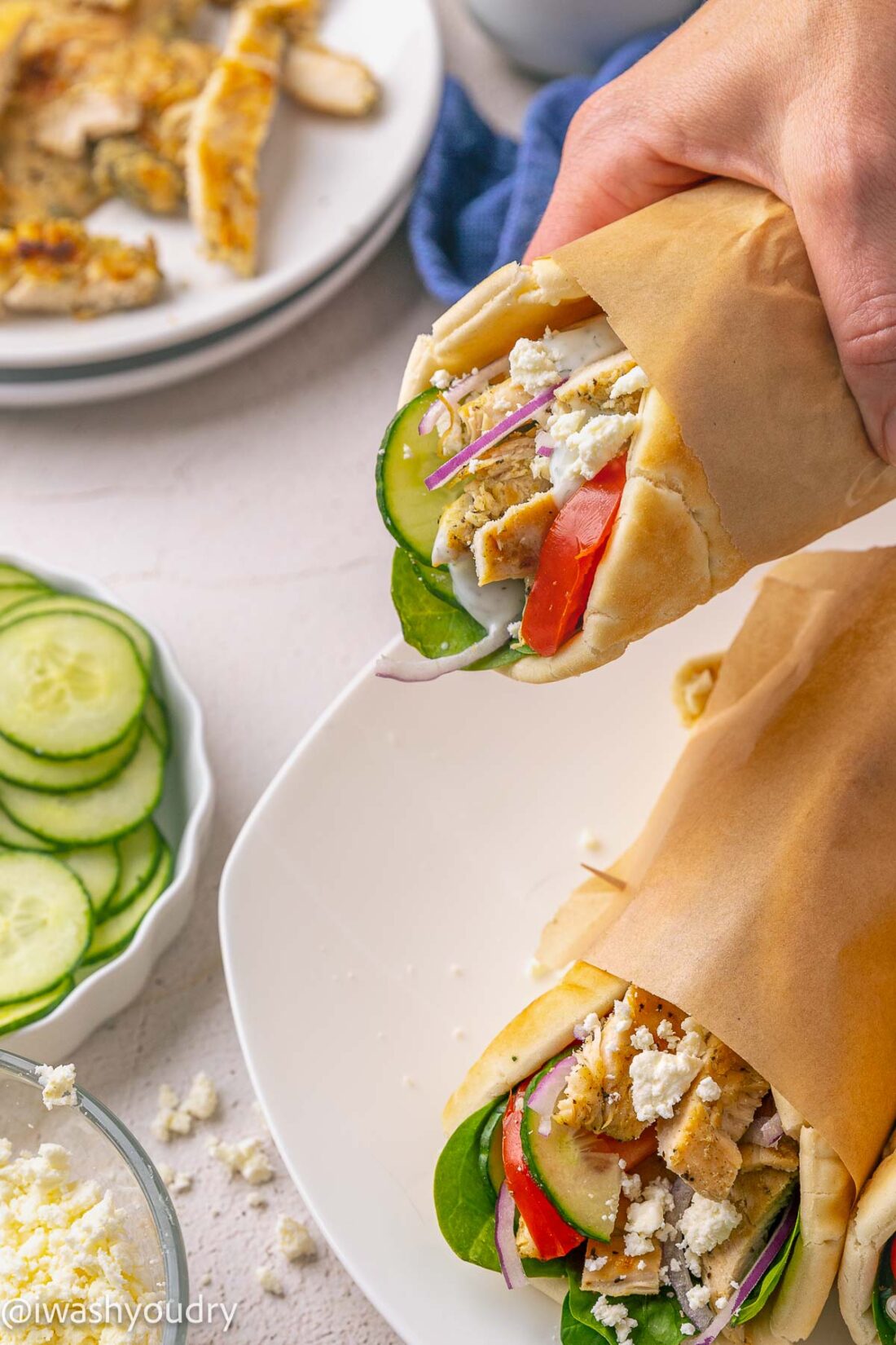 holding chicken souvlaki pita with cucumbers and tomatoes.