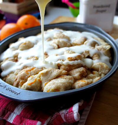 Icing being drizzled on top of a round pan of Orange Cinnamon Pull Apart