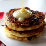 A close up of a display of three pancakes on a plate being topped with a syrup.