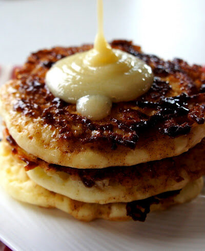 A close up of a display of three pancakes on a plate being topped with a syrup.