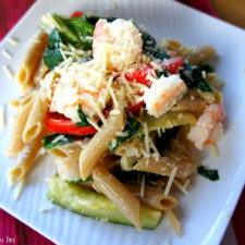 A close up of pasta displayed on a plate  topped with veggies, shrimp and cheese