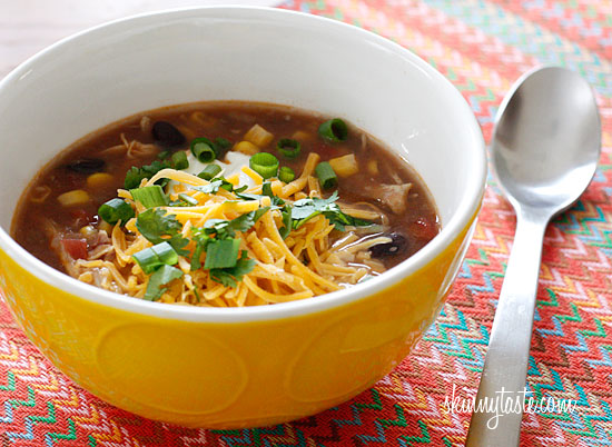 A bowl of Enchilada Soup on a table, topped with shredded cheese and cilantro