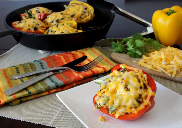 A stuffed bell pepper covered with melted cheese on a plate displayed on a table in front of a pan of more stuffed peppers