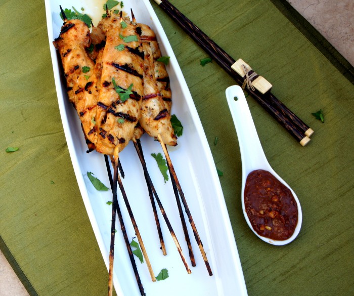 Thai Chicken Satay Skewers on a plate next to a small bowl of Spicy Peanut Dipping Sauce 